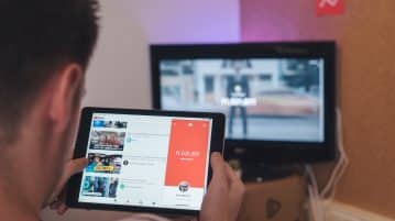 man browsing tablet sitting in front of TV