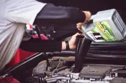 man refilling motor oil on car engine bay