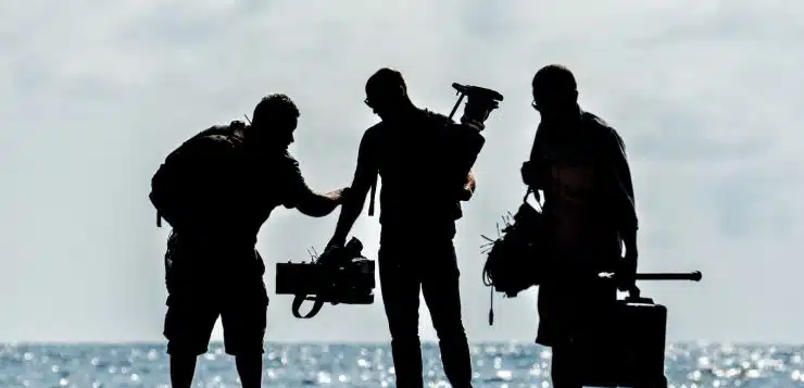 silhouette of men holding camera standing on sand near body of water during daytime